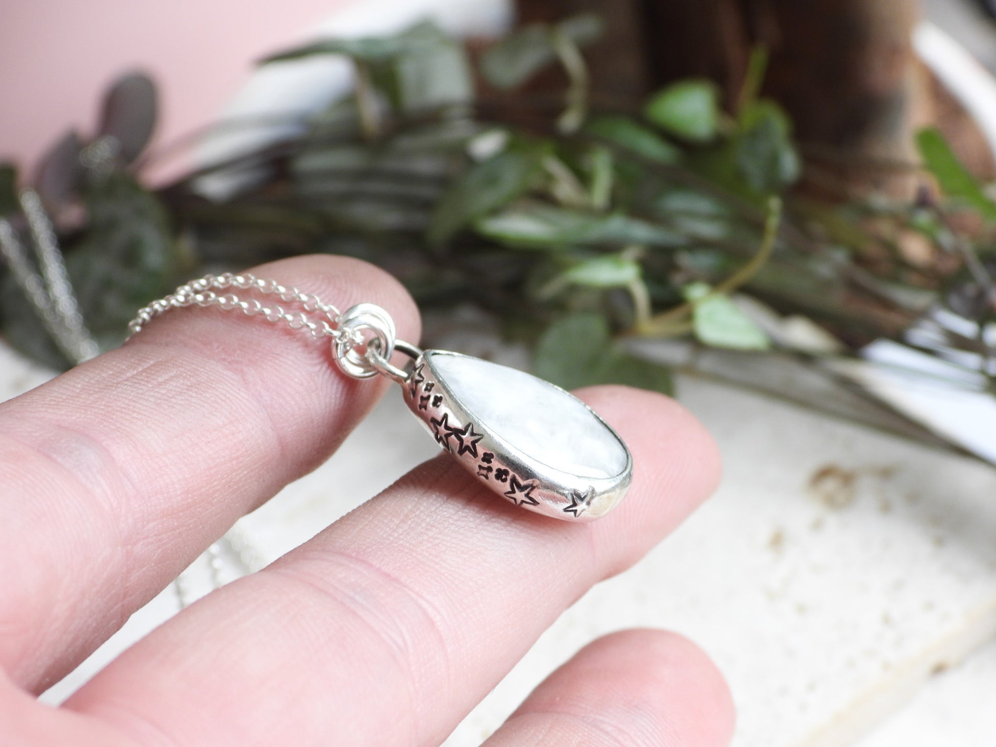 Silver necklace with a pendant held by a hand against a blurred natural background
