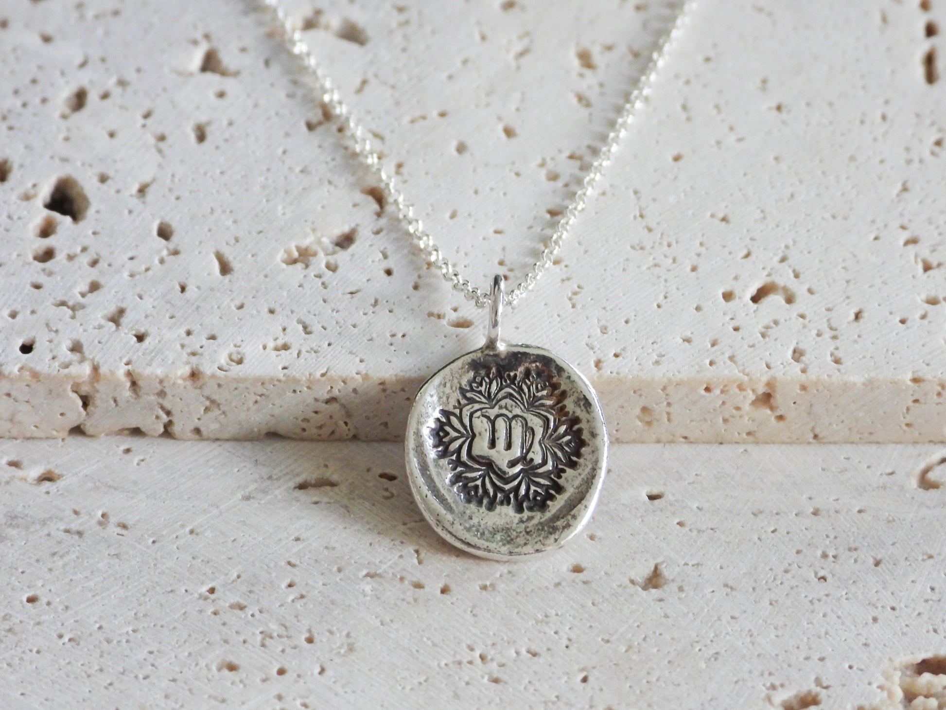Silver virgo necklace with a detailed pendant on a textured beige surface