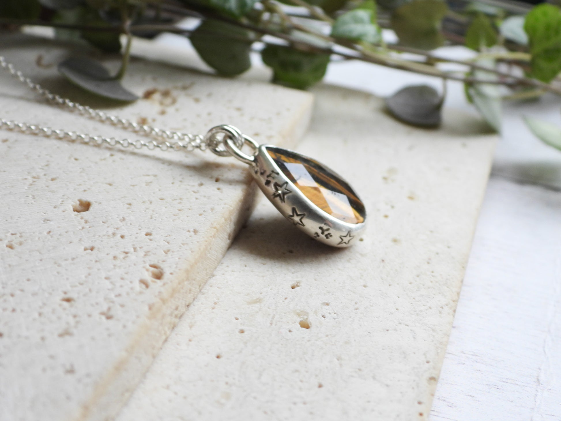 Silver tiger's eye pendant necklace on a textured surface with greenery in the background